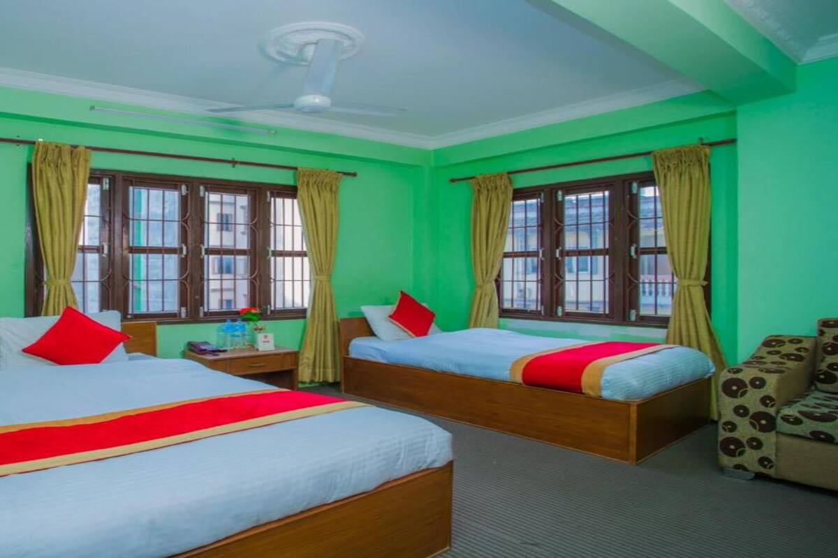 A hotel room with two single beds, a sofa, and a ceiling fan.