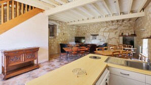 A rustic kitchen with a stone wall, wooden dining table, and a built-in stove. - Le Logis de Poëllier (Baugé-en-Anjou)