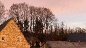 A stone building with a triangular roof, a gravel driveway, and a fenced area. - Le Logis de Poëllier (Baugé-en-Anjou)