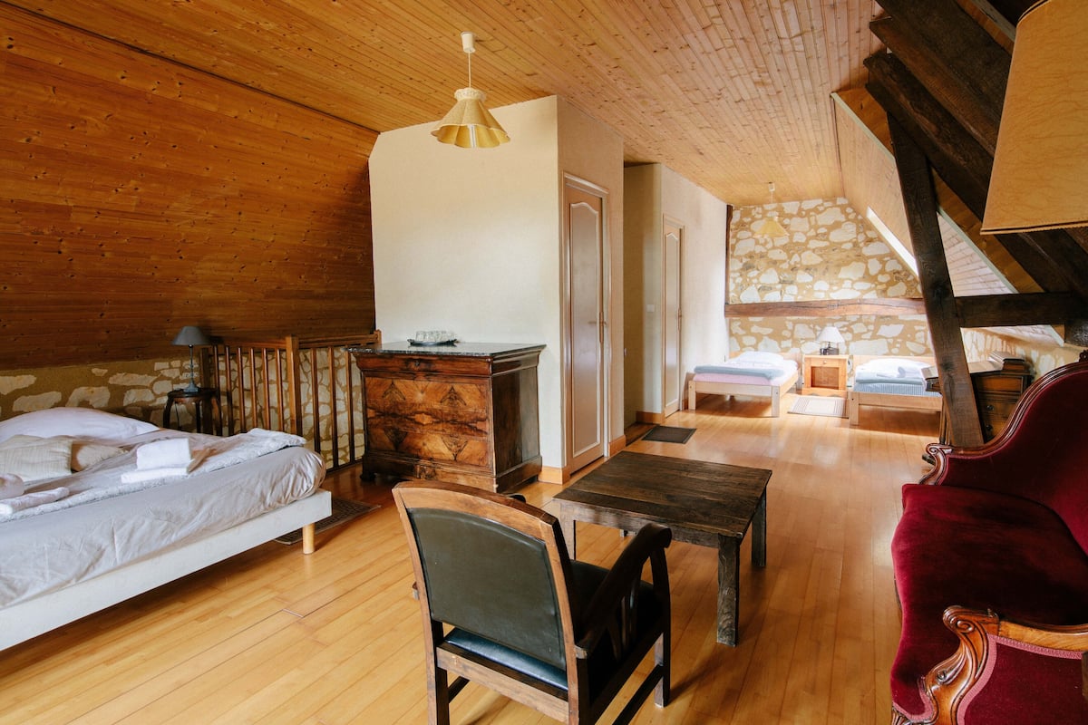 A cozy room with a bed, a wooden dining table, a red chair, and a stone wall.