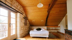 A bedroom with a wooden ceiling, a bed, a dresser, and a stone wall. - Le Logis de Poëllier (Baugé-en-Anjou)