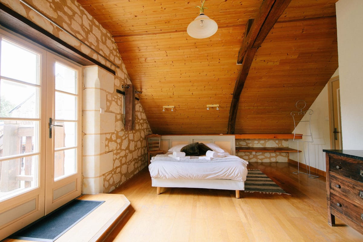 A bedroom with a wooden ceiling, a bed, a dresser, and a stone wall.