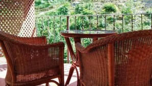 A balcony with wicker chairs and a glass table, overlooking a mountainous landscape. - Apartamentos Aguasaliu (Ponga)