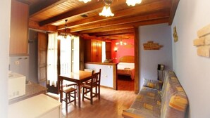 A cozy room with a wooden ceiling, a dining table with chairs, a sofa, and a small kitchen area with a refrigerator and a microwave. - Apartamentos Aguasaliu (Ponga)