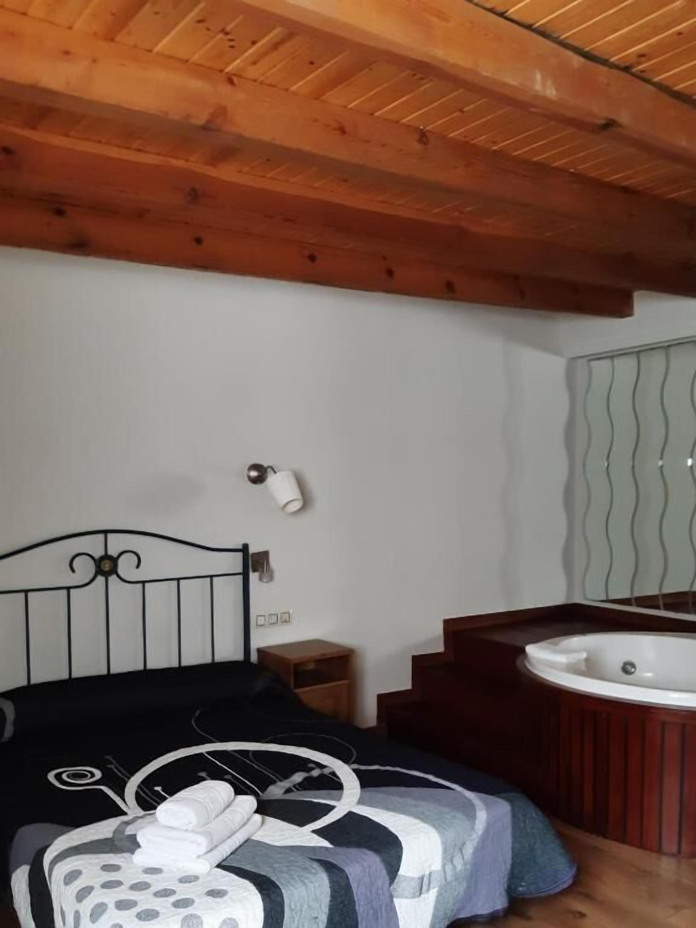 Ein Schlafzimmer mit Bett, Nachttisch, Wandlampe, einem Badezimmer mit Badewanne und Spiegel.