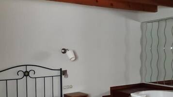 Un dormitorio con cama, mesita de noche, lámpara de pared, baño con bañera y espejo.