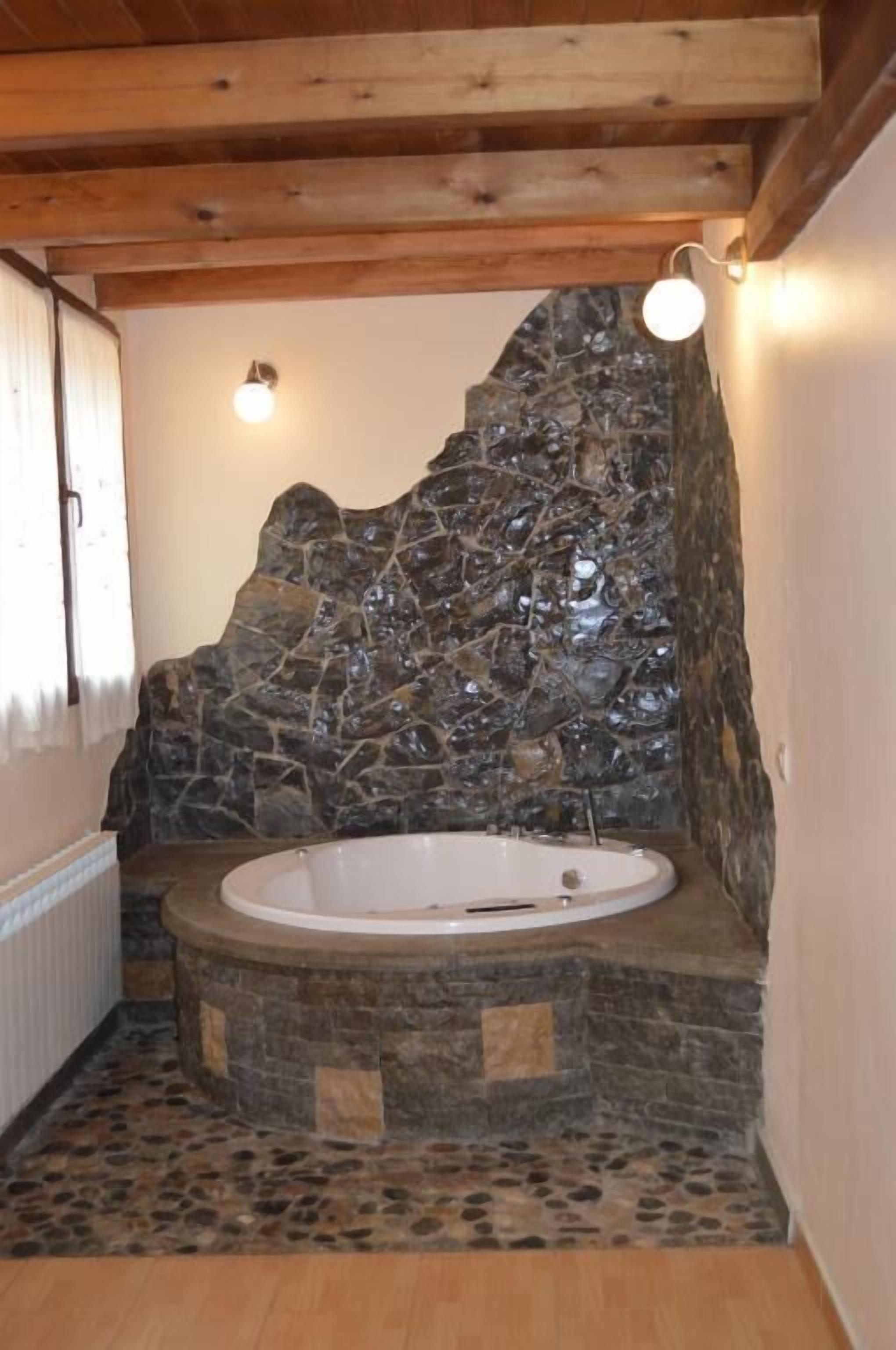 A bathroom with a stone wall, a freestanding bathtub, and a wooden ceiling.