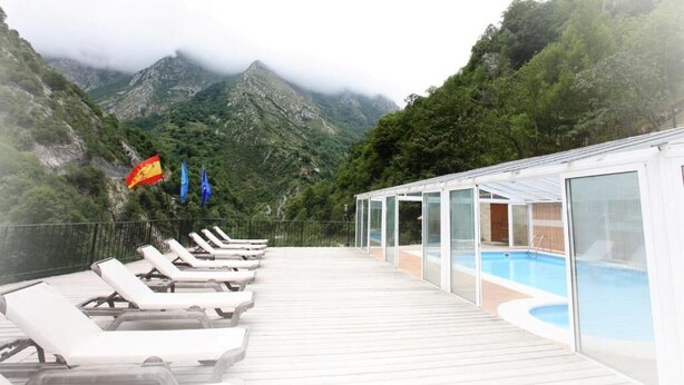 A deck with sun loungers overlooking a pool, surrounded by lush greenery and mountains. - Apartamentos Aguasaliu (Ponga)