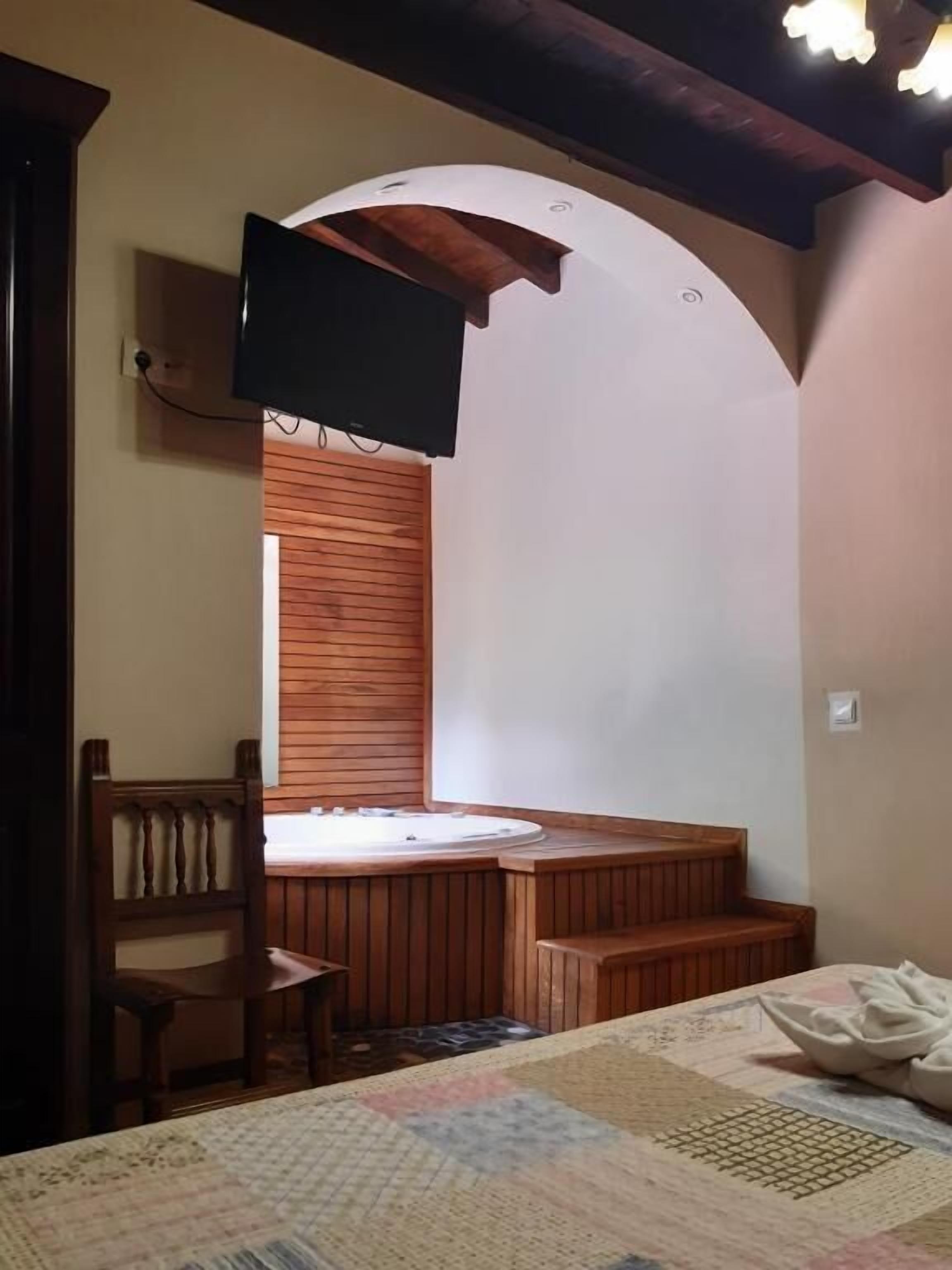A room with a wooden bench, a television mounted on the wall, and a window with wooden blinds.