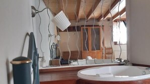 A modern bathroom with a freestanding bathtub, wooden beams on the ceiling, and a large mirror reflecting the room. - Apartamentos Aguasaliu (Ponga)
