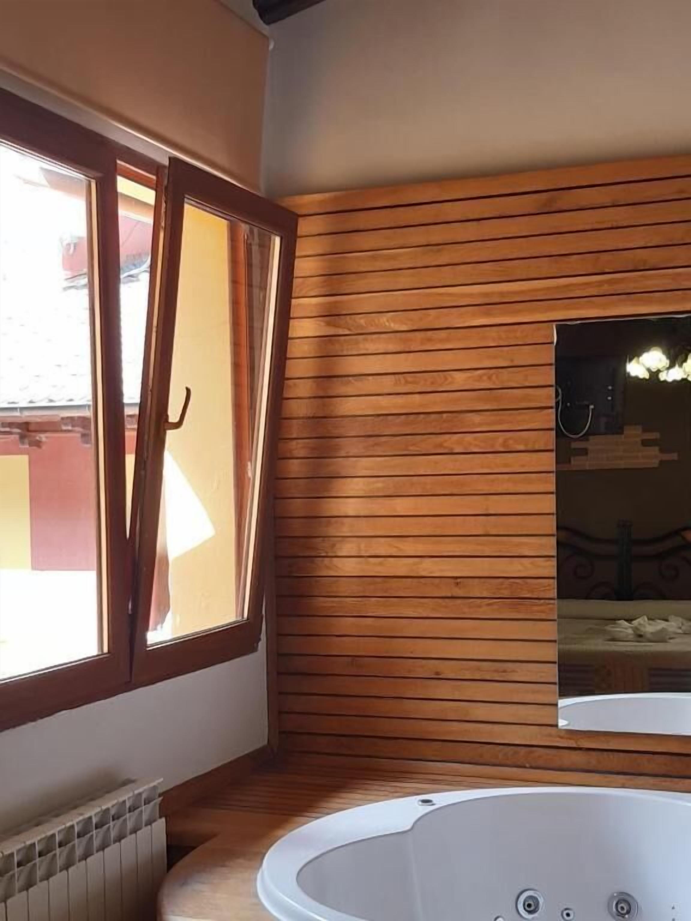 A modern bathroom with a wooden panel wall, a large window, and a freestanding bathtub.