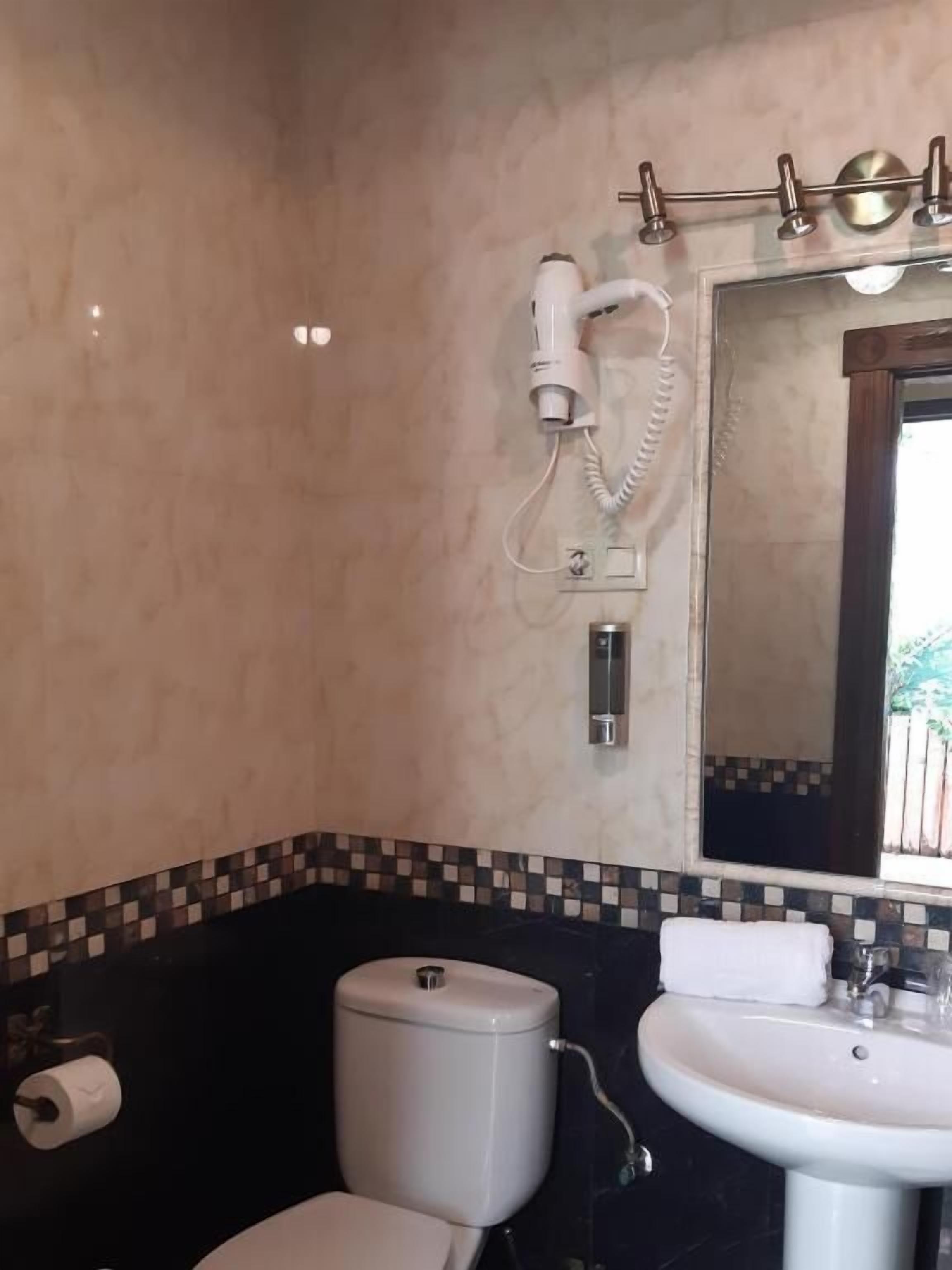 Un baño con inodoro, lavamanos y secador de pelo montado en la pared.