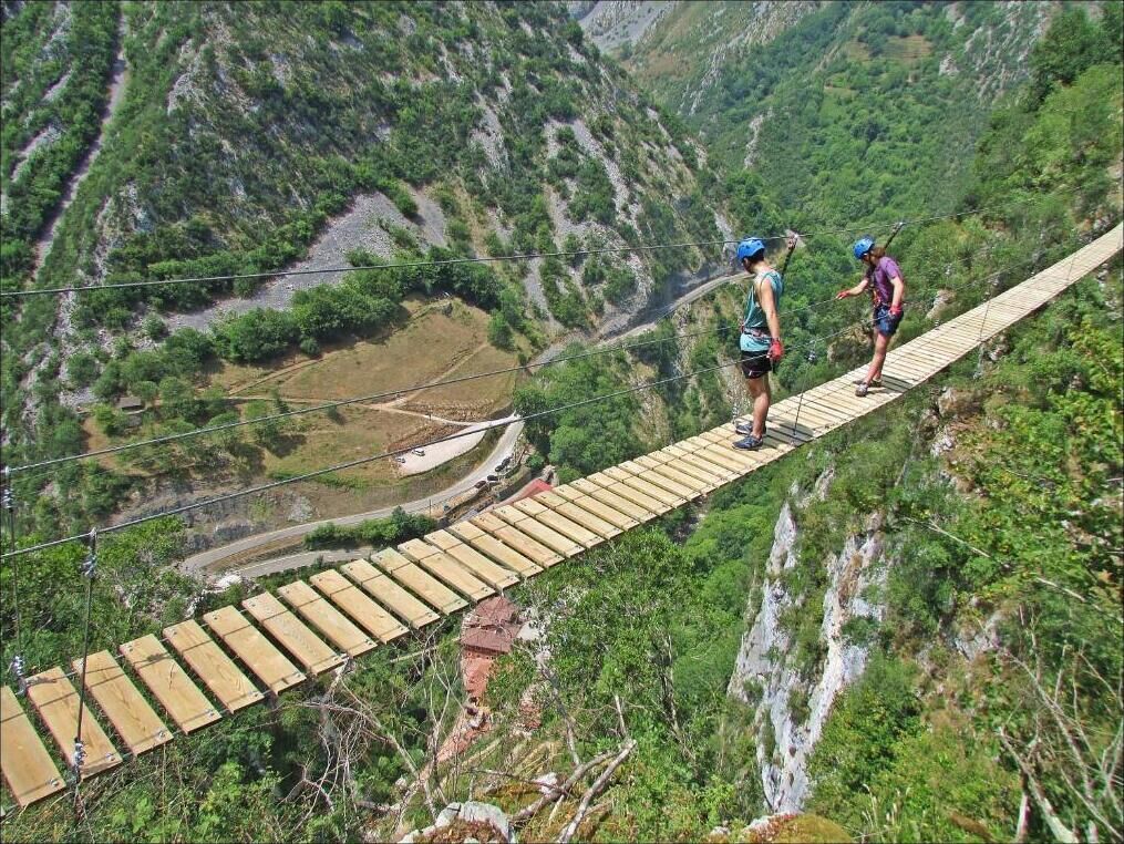 Un puente colgante de madera sobre un valle con vegetación exuberante y terreno rocoso.