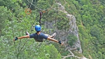A person bungee jumping with a safety harness and helmet, surrounded by dense green forest and rocky cliffs.