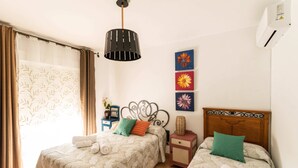 A hotel room with two beds, a wooden headboard, a nightstand, a lamp, and a window with curtains.