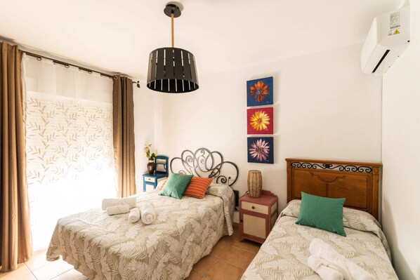 Habitación de hotel con dos camas, cabecera de madera, mesita de noche, lámpara y ventana con cortinas.