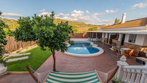 A pool area with a hammock, a patio, and a view of the surrounding landscape.