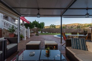 A covered patio with wicker furniture, a pool, and a view of the hills.