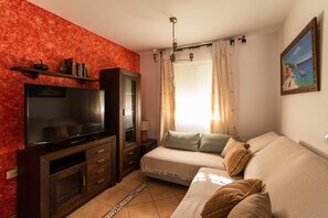 A living room with a flat-screen TV, wooden entertainment unit, sofa, and a painting on the wall.