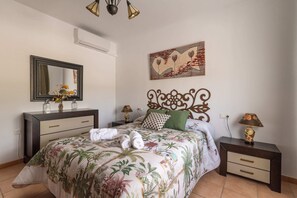 A bedroom with a bed, a dresser, a nightstand, a lamp, a mirror, and a wall art piece.