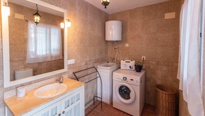 A compact bathroom with a sink, mirror, toilet, washing machine, and a towel rack.