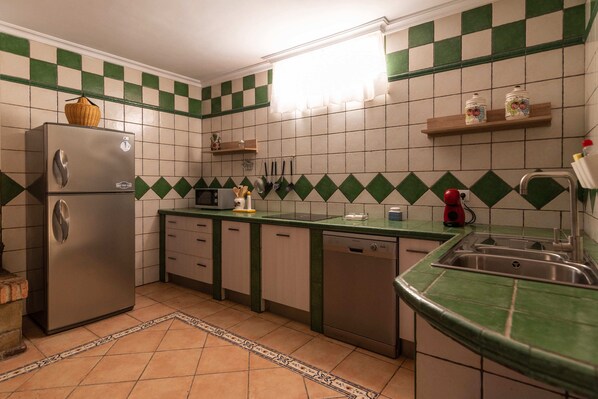 A kitchen with a refrigerator, dishwasher, and a microwave. There are green and white checkered tiles on the walls and a green countertop.