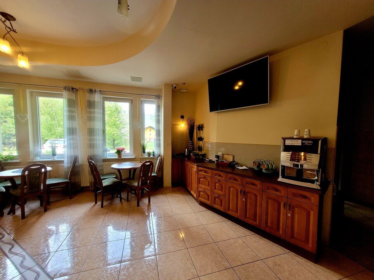 A kitchen with a coffee machine, a TV, and a dining area with chairs and a table.