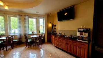 A kitchen with a coffee machine, a TV, and a dining area with chairs and a table.