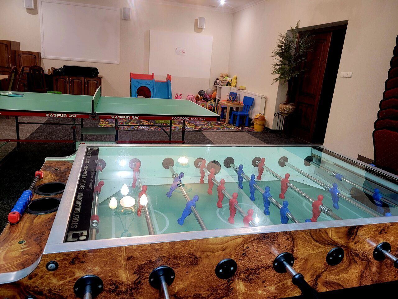 Ein Raum mit zwei Kicker-Tischen, Holzschränken, einer Whiteboard-Tafel und einer Topfpflanze.