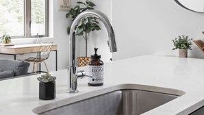 Une cuisine moderne avec un évier en acier inoxydable, une table à manger en bois et une grande fenêtre.