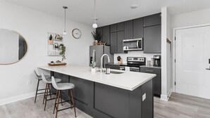 Une cuisine moderne dotée d’un grand îlot central, de meubles de couleur sombre et de plans de travail blancs.