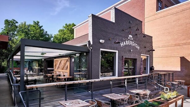 An outdoor patio area with tables and chairs, a wooden pergola, and a brick building with the name "HABERDISH" visible. - Historic NoDa Mill House • Steps to Shops & Dining (Charlotte)