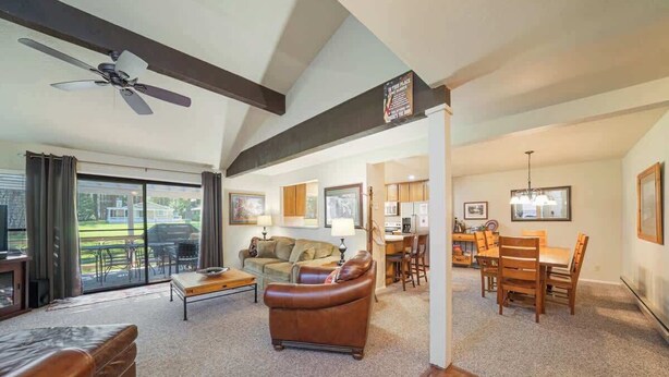 A spacious living room with a large window, a ceiling fan, a brown leather sofa, a coffee table, and a dining area with wooden furniture. - Caddyshack - 35 Aspen Circle (Plumas Eureka)