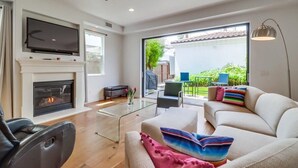 Una sala de estar moderna con chimenea, un televisor de pantalla plana, un ventilador de techo y un amplio ventanal con vistas al exterior.