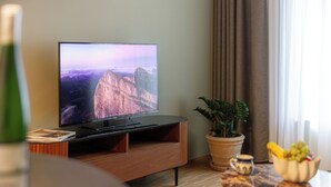 Een televisie op een houten standaard, een potplant, een fruitschaal en een klein tafeltje met een kop.