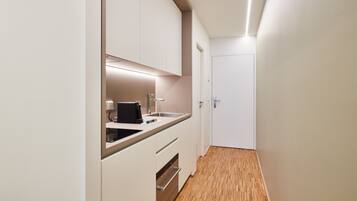 A narrow hallway with a kitchen area on the left, featuring white cabinets, a countertop, and a sink.