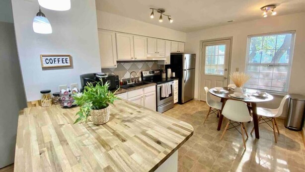A modern kitchen with a wooden countertop, stainless steel appliances, and a dining area with white chairs. - 2 King Beds + quiet + ground floor A (Norfolk)