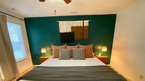 A bedroom with a bed, two bedside tables, a wall-mounted lamp, and a window with blinds. - 2 King Beds + quiet + ground floor A (Norfolk)