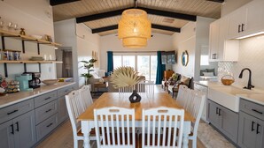 Una cocina amplia con una mesa de comedor de madera, sillas blancas y una lámpara colgante.