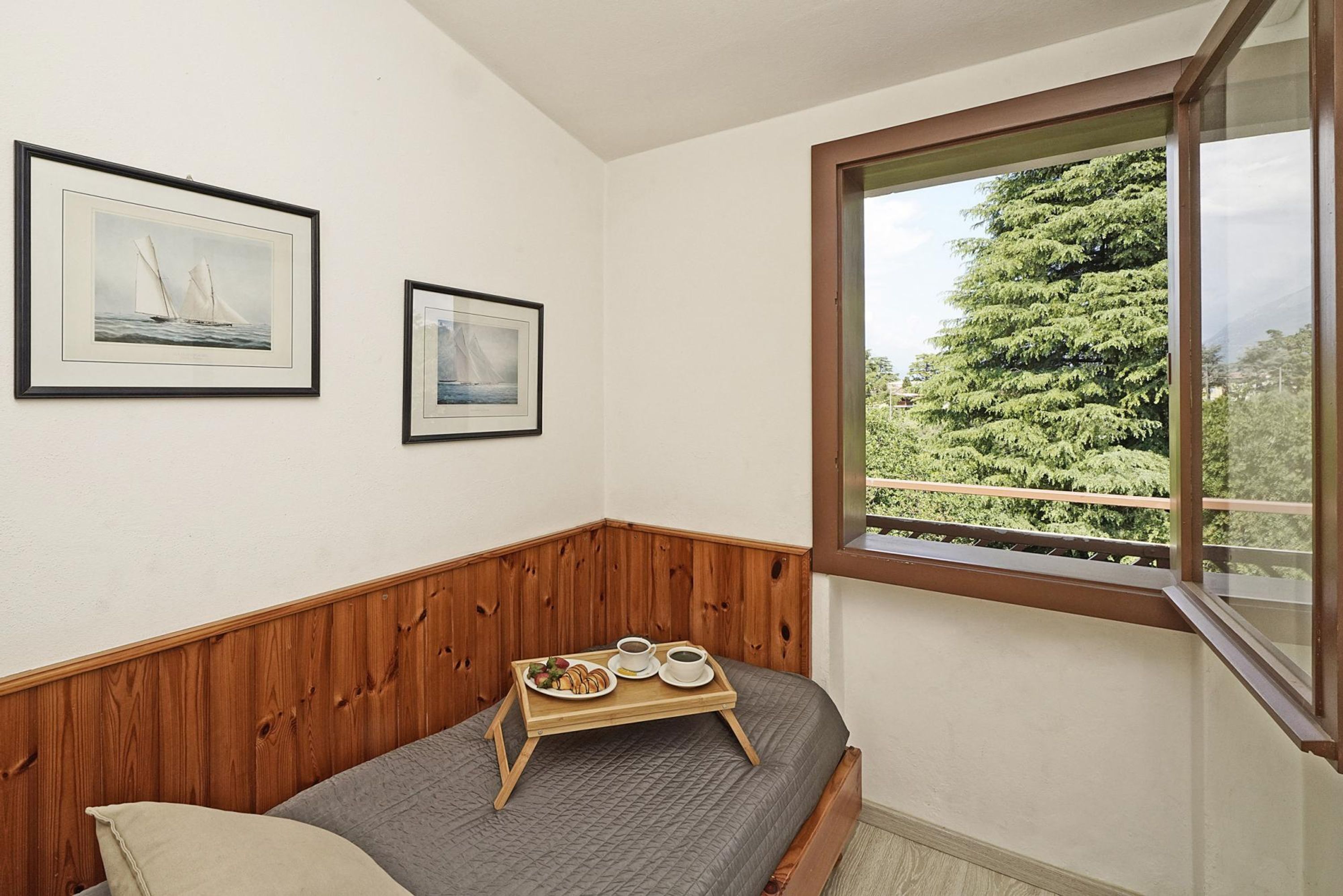 Une chambre à coucher avec une tête de lit en bois, un lit recouvert d’une couverture grise, un plateau avec le petit-déjeuner et une fenêtre donnant sur des arbres.