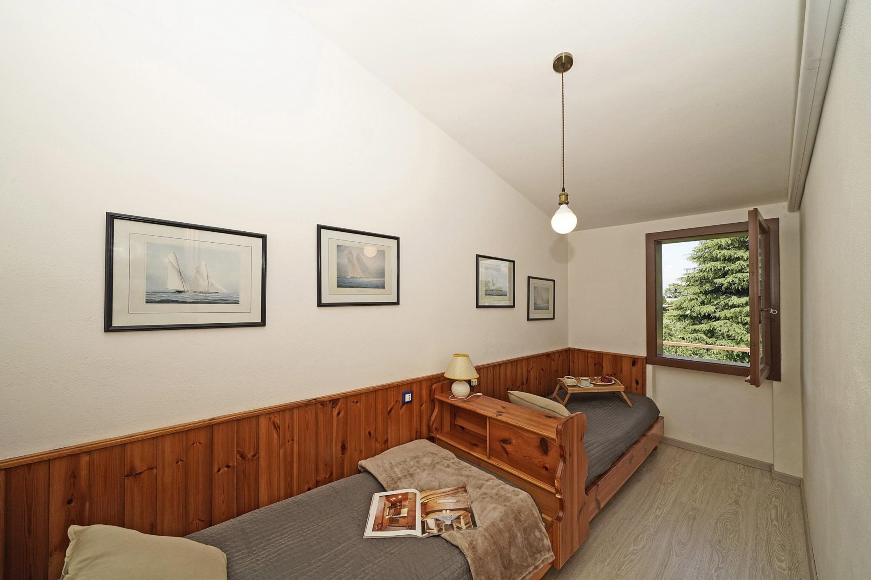 Una stanza piccola e accogliente con una testiera di legno, un letto singolo, un comodino con una lampada e quadri appesi al muro.