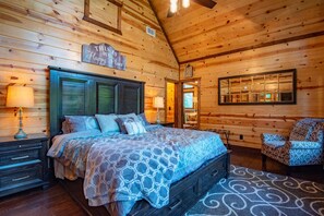 Un dormitorio rústico tipo cabaña de madera con una cama grande, paredes de madera, un espejo y una silla.