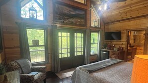 A log cabin bedroom with a bed, a chair, a desk, and a television.