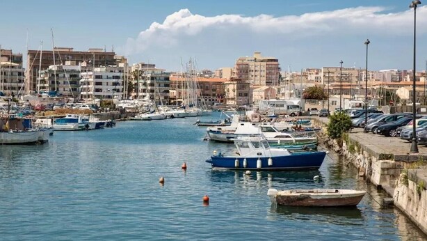 A marina with boats docked, surrounded by buildings and a clear sky. - Elizabeth House (Siracusa)