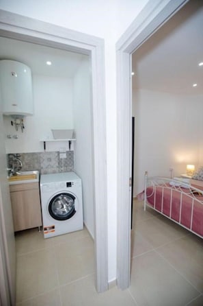Une petite pièce comprenant un lave-linge, un lit et une kitchenette.