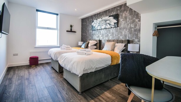 A modern bedroom with two beds, a large window, and a grey accent wall with a floral painting. - Apartment 4 - The Crescent (York)