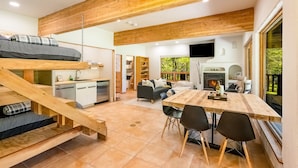 A modern interior with a loft bed, kitchen, dining area, and fireplace. - Private Oasis on 15 Acres, Gas Firepit, Large Decks, Private Feel, EV/RV Hookups (Angel Fire)