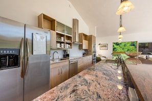 A modern kitchen with stainless steel appliances, wooden cabinets, granite countertops, and a large window with a view of greenery.