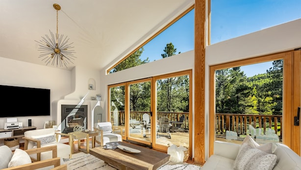 A spacious living room with a large TV, wooden furniture, and a view of the outdoors. - Private Oasis on 15 Acres, Gas Firepit, Large Decks, Private Feel, EV/RV Hookups (Angel Fire)