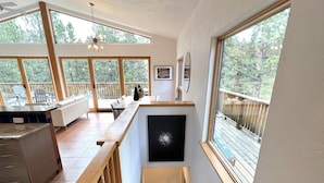 A spacious kitchen with a long countertop, wooden railing, and a view of the outdoors through large windows. - Private Oasis on 15 Acres, Gas Firepit, Large Decks, Private Feel, EV/RV Hookups (Angel Fire)